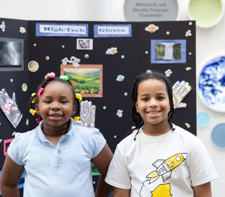 Two Buffalo Public Schools students stand in front of a poster presentation about high tech gloves